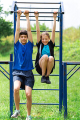 Fototapeta premium teenage boy and girl exercising outdoors, sports ground in the yard, they posing at the horizontal bar, healthy lifestyle