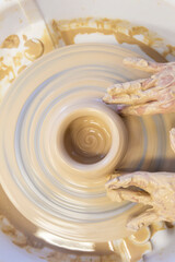 Close-up of a potter's hands with an item on a potter's wheel. Working with clay. Clay workshop. Craft training.