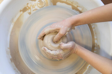 Close-up of a potter's hands with an item on a potter's wheel. Working with clay. Clay workshop. Craft training.