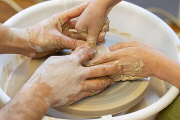 The potter teaches the child the craft. Close-up of a potter's hands and a child's hand with an item on a potter's wheel. Working with clay. Clay master class.