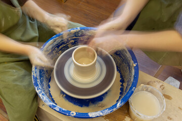 Earthenware on a potter's wheel and the hands of a potter, blurred in motion. Pottery training.