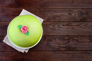 Princess cake with green marzipan cover and pink rose decoration, on dark wooden background,...