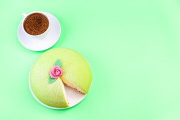 Princess cake with green marzipan cover and pink rose, served with cup of coffee, on green...
