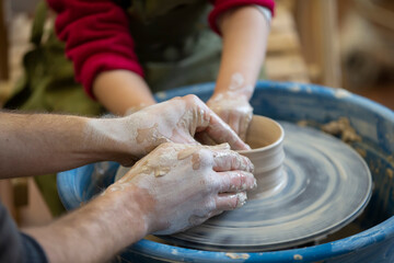 The potter teaches the craft to the child. Close-up of a potter's hands and a child's hand with a product on a potter's wheel. Working with clay. Clay master class.
