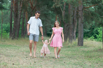Obraz premium Husband, wife and their little daughter for a walk in the park. Happy dad and mom are walking through the woods with their one-year-old daughter.
