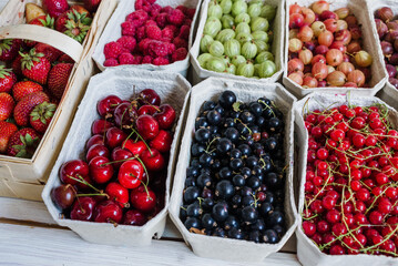 Healthy summer fruit variety. Sweet cherries, strawberries, blackberries, gooseberries, red currant and black currant in paper boxes over a rustic wooden background. Top view