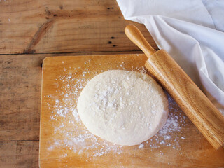 Fresh raw dough with rolling pin on wooden cutting board for pizza or bread on the table.