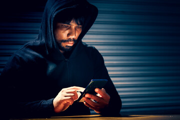 Mysterious man in a hoodie on dark background. Dangerous criminal. Silhouette of man in the hood,...