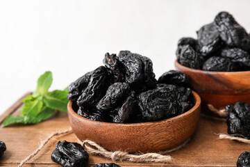Bowl with tasty prunes on light background, closeup