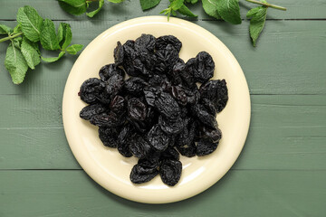 Plate with tasty prunes on color wooden background