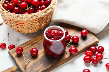 Basket with ripe cherry ad jam on light background, closeup