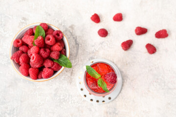Glass of delicious lemonade and bowl with raspberry on light background
