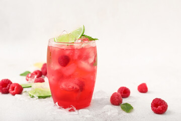Glass of cold lemonade with raspberry on light background