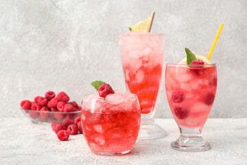 Glasses of cold lemonade with raspberry on light background