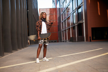 Portrait of modern african girl with skateboard. Young stylish woman using the phone.