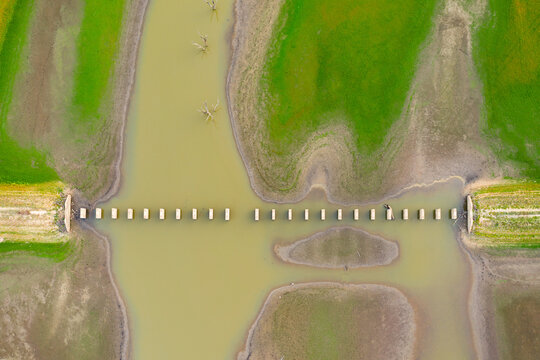 Looking straight down on a row of concrete bridge pillars crossing a river