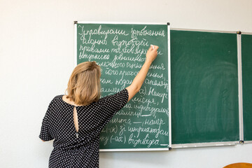 The student student writes with chalk on the blackboard in the classroom
