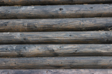The wall of an old wooden house made of darkened weathered logs. Traditional Russian log hut.
