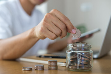 Saving money concept. Female hand putting money coin stack in the jar for the future, growing business, education and retirement on office desk at home. She felt that saving money made his life safe.
