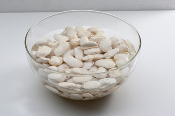 Bol de alubias en agua para la elaboración de fabada sobre fondo blanco. Bowl of beans in water for the preparation of fabada on a white background.