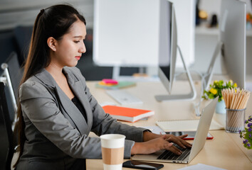 Fototapeta na wymiar Young attractive Asian woman in grey business suit working on laptop in modern looking office. Concept for modern office lifestyle