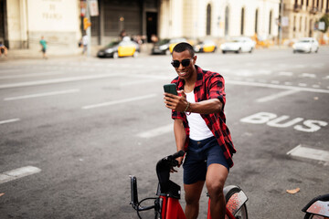 Fototapeta na wymiar Portrait of handsome african man using electric bike in the city. Happy young man using the phone..