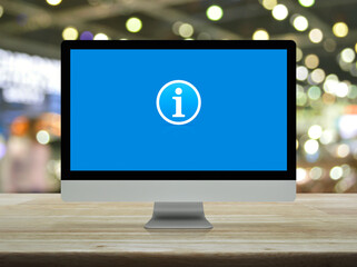 Information sign flat icon on desktop modern computer monitor screen on wooden table over blur light and shadow of shopping mall, Business customer service and support online concept