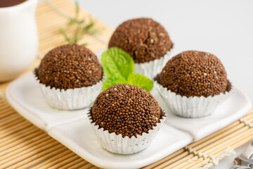 Perilla seed mixed with Jaggery palm sugar and mold into a ball place on a white plate decorated with mint leaves on a bamboo mat with spoons and forks.