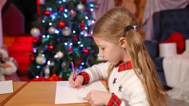 Portrait of a lovely little girls indoors at Christmas. Cute children writing a letter to Santa. Beautiful small girl drawing a picture on xmas background at home
