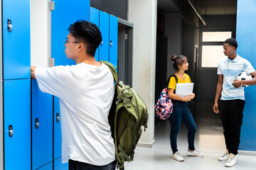 Teen asian high school student putting books away in lockers. Teenagers talking in school corridor.