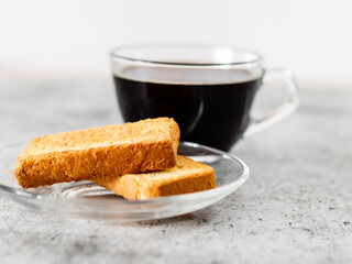 Fototapeta na wymiar Closeup shot of rusk in saucer with defoused black coffee on background.