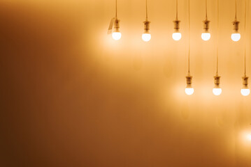 Lots of glowing bulbs hanging in a row against a yellow wall, copy space. Minimalistic illuminated electrical equipment.