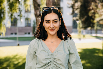 Young brunette woman outdoors in a park, smiling, looking at camera.
