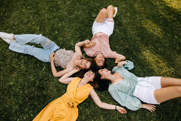 Group of four young women lying on green grass, outdoors, in a park, smiling.