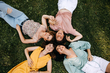 Group of four young women lying on green grass, outdoors, in a park, laughing.