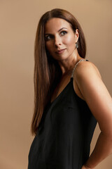 Portrait of a beautiful woman with long hair in a stylish black dress. Brown background. Vertical.