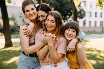 Closeup portraits of four young women hugging and laughing, outdoors.