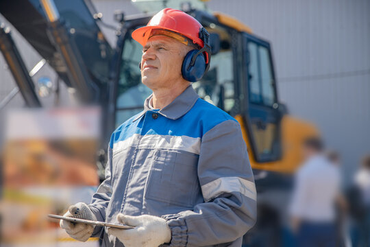 Industrial worker male senior in helmet holds tablet computer on background of production of escovator factory.