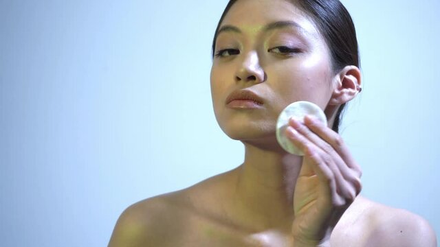 young asian woman cleansing face with cotton pad on blue