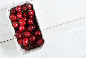 Fresh organic cherries in paper box over white wooden rustic background. Top view. Fresh ripe cherries. sweet cherry