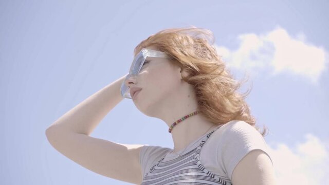 low angle view of redhead teenage girl in sunglasses against blue sky