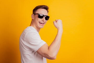 Naklejka premium Portrait of confident sportive athlete guy show biceps muscle raise hand on yellow background