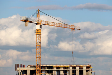 Construction crane and unfinished residential building on background of blue sky with white clouds. Housing construction, apartment block in city