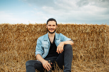 Naklejka na ściany i meble Outdoor portrait of young man in denim jacket, sitting in the wheat field.