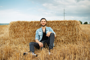 Naklejka na ściany i meble Outdoor portrait of young smiling man, sitting in the wheat field.