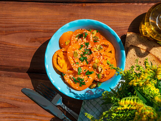 Yellow tomatoes salad with rye bread slices in blue ceramic bowl top view. Ripe fresh colorful vegetables mixed sliced greens with olive oil vinegar pumpkin sesame flax seeds on wooden background.