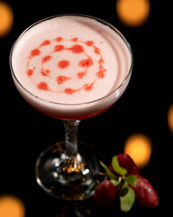 Festive alcoholic drink with froth In cocktail glass on black blurred background with bokeh. Vertical format. Copy space. Soft focus.