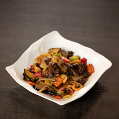 Plate with stir-fried meat and vegetables on wooden background. Oriental Cuisine. Copy space. Soft focus.