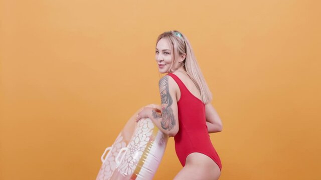 Sexy blonde woman in one piece swimsuit playing with a swim ring. Throwing the swim ring and catching it.