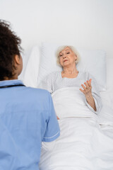 Obraz premium Senior patient talking to african american nurse in hospital ward